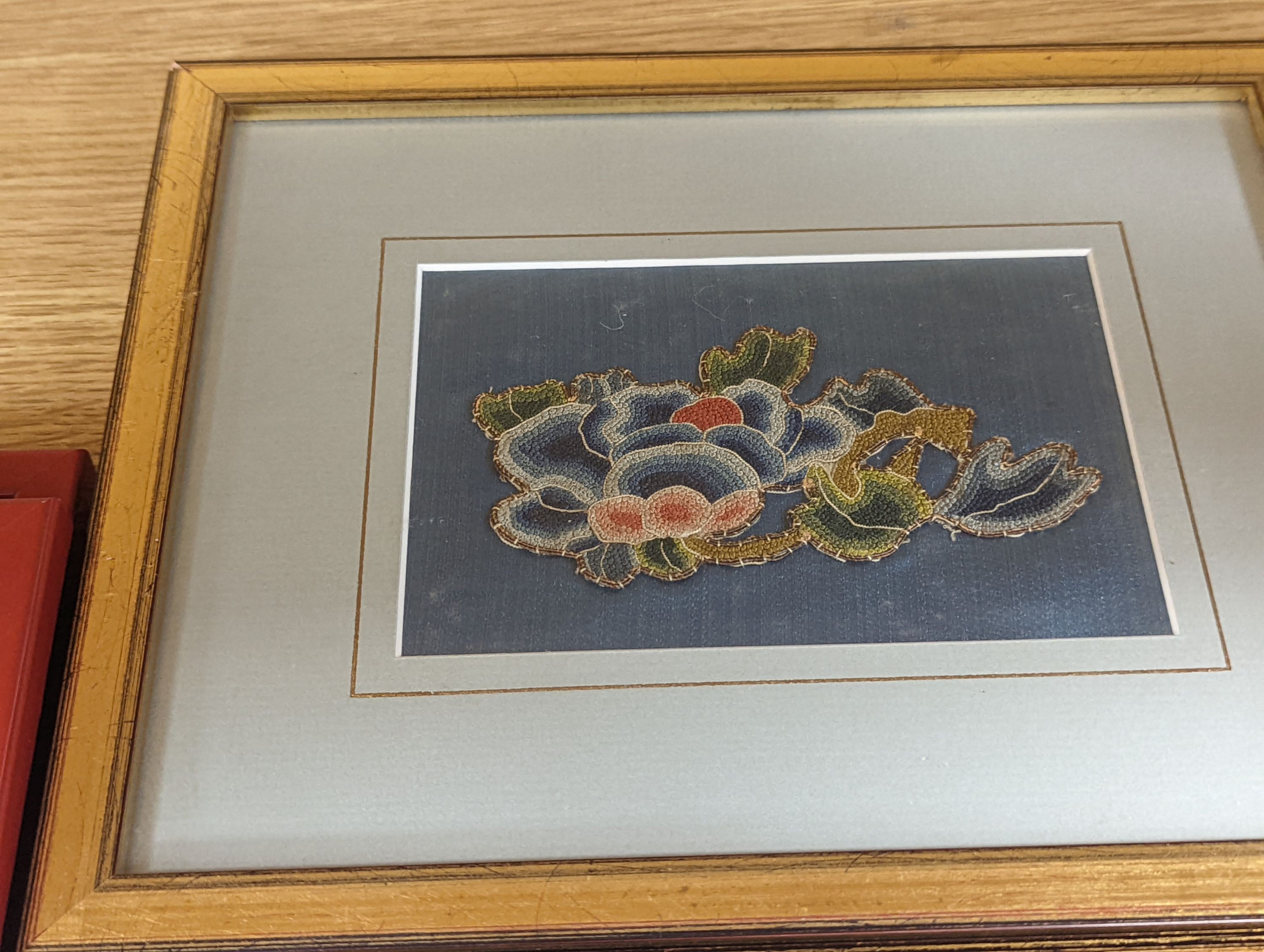 A set of four Chinese silk embroidered motifs, a pair of floral silk motifs and a later pair f sleeve bands, all framed